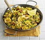 Seafood paella in a large silver pan with lemon wedges