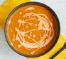 A bowl of squash , red pepper and harissa soup, topped with creme fraiche