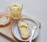 Vegan mayonnaise in a jar, with some spread on a slice of bread alongside